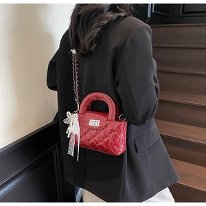 Detail of red quilted patent leather bag with silver twist lock and lace pearl bow charm