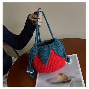 Detailed view of handmade red strawberry crochet bag with blue leaves on a wooden table