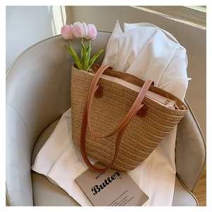 Detail of hand-woven straw tote bag with brown leather handles on a grey chair