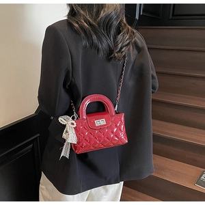 Detail of red quilted patent leather bag with lace bow and pearl charm accent