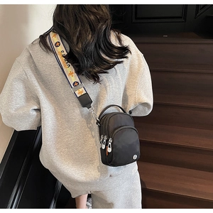 Vue arrière d'un sac bandoulière noir en tissu avec sangle décorative sur un escalier bois