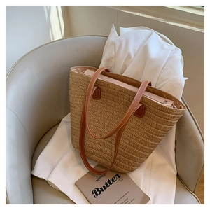 Detail of hand-woven straw tote with brown leather handles on a minimalist sofa