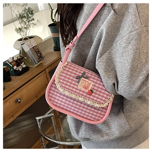 Detail of pink gingham crossbody bag with lace trim, bow, and strawberry charm on model