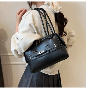 Detail of a black glossy leather shoulder bag with silver metal lock on a model