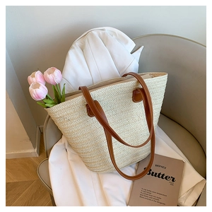 Large beige woven straw tote bag with brown leather handles resting on a white blazer