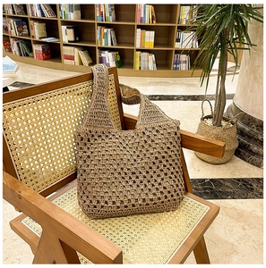 Detail of a brown hand-woven hollow straw hobo bag placed on a rustic wooden chair