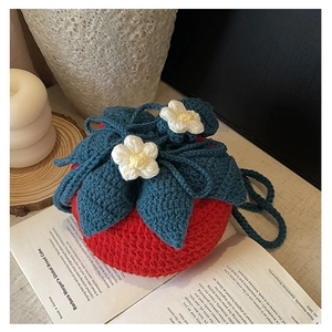 Detail of handmade crochet strawberry knit bag with floral accents on an open book