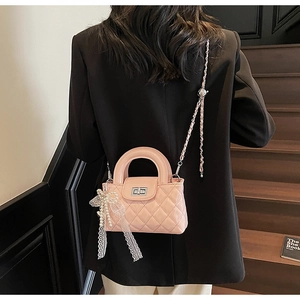 Pink quilted leather jelly bag with pearl bow charm worn by a model in a casual pose
