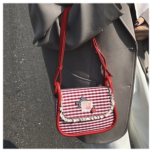 Detail of red gingham canvas bag with lace trim, bow, and strawberry charm on shoulder