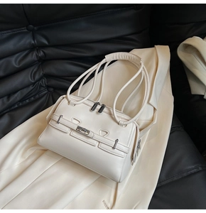 Close-up of cream underarm bag with silver buckle on elegant blazer and leather sofa