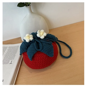 Detailed view of handmade red tomato-shaped knitted bag with green leaves and white flowers