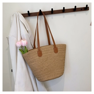 Detail of woven straw tote bag featuring brown leather handles on a wooden rack