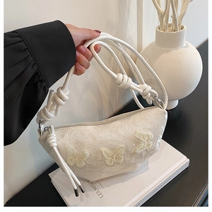 Detailaufnahme der weißen Halbmondtasche mit Schmetterlingsstickerei und Knotengurt