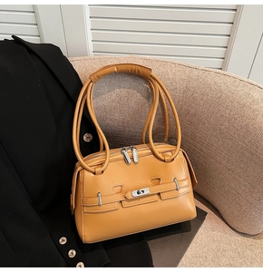 Close-up of ginger leather handbag with metallic twist lock on a beige sofa
