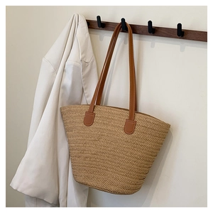 Detail of hand-woven straw tote bag with brown leather strap and white stitching