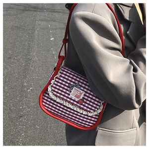 Detail of red checkered canvas shoulder bag with lace trim and strawberry charm on a model