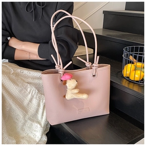 Detail of pink lychee leather tote bag with cute puppy pendant on a black staircase