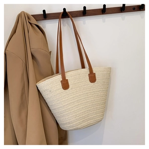 Detail of handwoven straw tote featuring premium brown leather handles and stitching