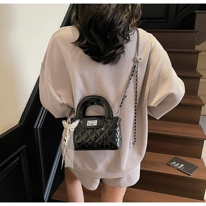 Detail of black quilted chain bag with shiny finish and delicate pearl lace bow charm