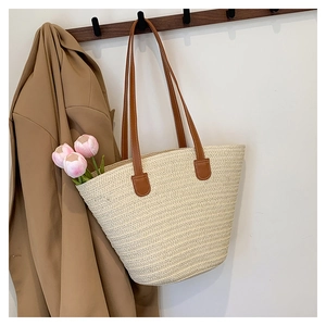 Detail of woven straw tote bag with brown leather straps hanging next to a tan blazer