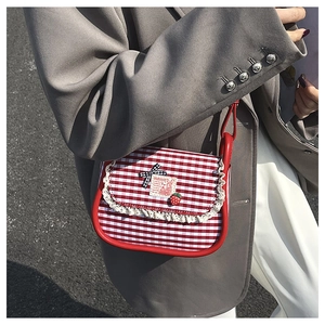 Close-up of red plaid canvas crossbody bag with lace trim and strawberry charm on model