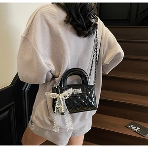 Close-up of black quilted patent leather bag with silver chain and lace pearl bow charm