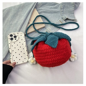 Detail of red knitted tomato shoulder bag with green leaves and white floral accent