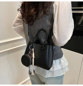 Detail view of black litchi grain bucket bag with adjustable strap and coin purse charm