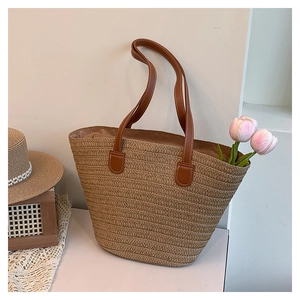 Detail of straw woven tote bag featuring brown leather handles and premium stitching