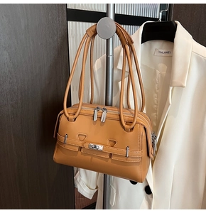 Close-up of ginger yellow leather handbag featuring silver twist lock and dual handle straps