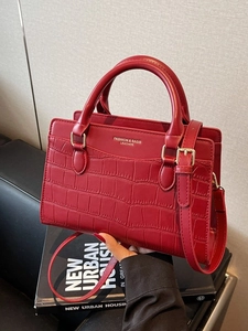 Elegant red crocodile embossed tote bag with gold hardware on a stylish black sofa