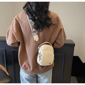 Détail d'un sac bandoulière en nylon crème avec trois fermetures éclair et sangle large