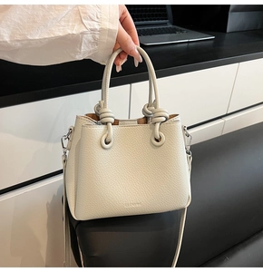 Close-up of beige lychee pattern leather bucket bag with knotted handle and metal logo