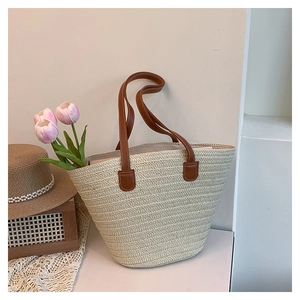 Detail of handwoven cream tote bag with sturdy brown leather handles on a summer desk
