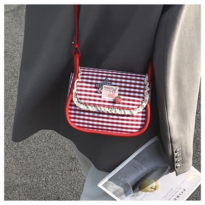Detail of red gingham canvas crossbody bag with lace edges and strawberry charm