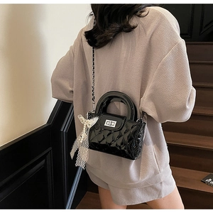 Close-up of black quilted patent leather bag with round handle and silver chain strap