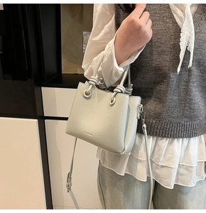 Detail of light green litchi texture bucket bag with knotted handle and brand logo