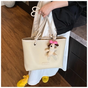 Detail of off-white lychee grain tote bag with knotted rope handle and plush dog charm