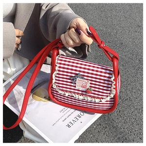 Detail of gingham crossbody bag featuring lace trim, strawberry charm and bow accent