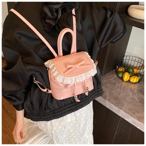 Detail of pink patent leather backpack featuring delicate white lace trim and bow accent
