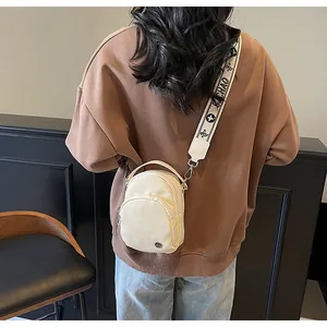 Détail du sac bandoulière en nylon crème avec large sangle florale sur un sweat marron