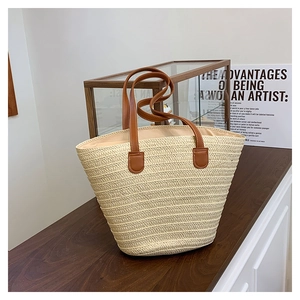 Detailed close-up of large straw tote bag featuring brown leather handles and beige weave