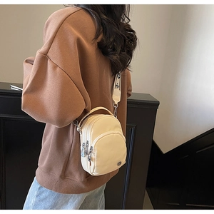 Détail du sac bandoulière en nylon crème avec trois poches zippées et large sangle à motifs