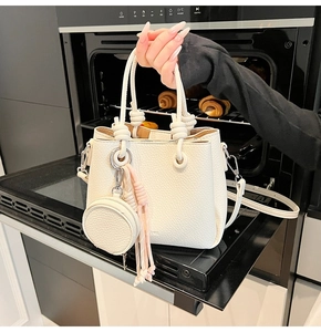 Close-up of cream white bucket bag with knot handle and round coin purse charm