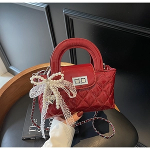 Detail of red quilted patent leather handbag with silver clasp and pearl bow charm
