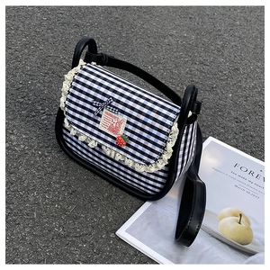 Detail of plaid canvas crossbody bag with lace edges and a 3D strawberry charm