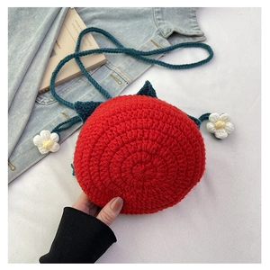 Close-up of handmade red tomato crochet shoulder bag with blue strap and floral charms