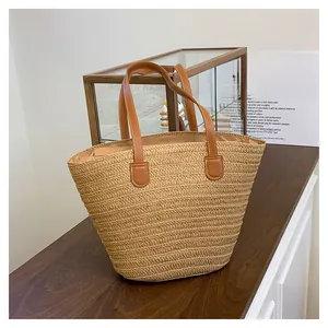 Detail of hand-woven straw tote bag featuring premium brown leather handles and sturdy stitching