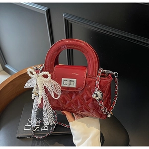 Close-up of red patent leather quilted handbag with pearl bow charm and metal chain