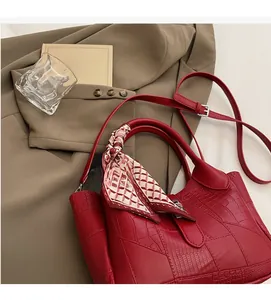 Detail of red croc-embossed bucket bag with decorative silk scarf and thin shoulder strap